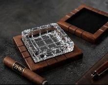 Square crystal cigar ashtray set into a dark wood base with a cigar and cutter alongside
