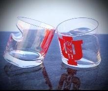 Two tilted old fashioned cigar glasses with red insignia, reflected on a dark surface