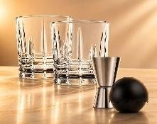 Faceted rocks glasses with a stainless jigger and a black chilling sphere on a warm wood surface