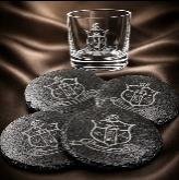 Round black slate coasters engraved with a fraternity crest, whiskey glass behind