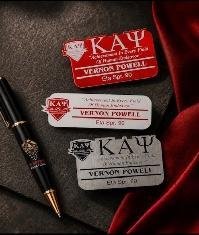 Red, white and silver engraved Kappa Alpha Psi name tags arranged with an engraved pen on dark velvet